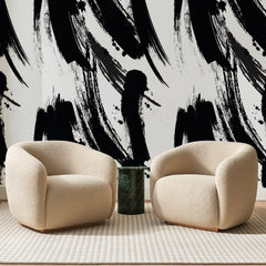 Papier peint panoramique Coups de Pinceau Noirs, posé sur toute la paroi d'un salon, derrière deux fauteuils en bouclette crème et un guéridon en marbre vert
