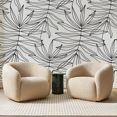 Papier peint panoramique Palmes à l'Encre Noire, posé sur toute la paroi d'un salon, derrière deux fauteuils en bouclette crème et un guéridon en marbre vert