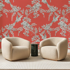 Papier peint panoramique Branches et Oiseaux Corail, posé sur toute la paroi d'un salon, derrière deux fauteuils en bouclette crème et un guéridon en marbre vert