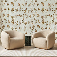 Papier peint panoramique Rameaux d'Automne Brun Doré, posé sur toute la paroi d'un salon, derrière deux fauteuils en bouclette crème et un guéridon en marbre vert