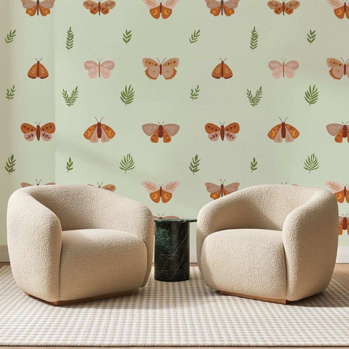 Papier peint panoramique Papillons Terracotta sur Vert Amande, posé sur toute la paroi d'un salon, derrière deux fauteuils en bouclette crème et un guéridon en marbre vert