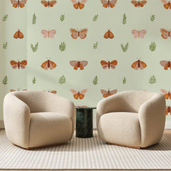 Papier peint panoramique Papillons Terracotta sur Vert Amande, posé sur toute la paroi d'un salon, derrière deux fauteuils en bouclette crème et un guéridon en marbre vert