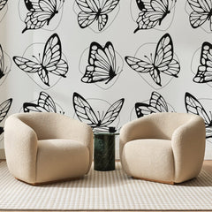 Papier peint panoramique Papillons Noirs sur Blanc, posé sur toute la paroi d'un salon, derrière deux fauteuils en bouclette crème et un guéridon en marbre vert