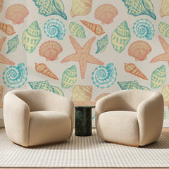 Papier peint panoramique Coquillages Pastel sur Crème, posé sur toute la paroi d'un salon, derrière deux fauteuils en bouclette crème et un guéridon en marbre vert