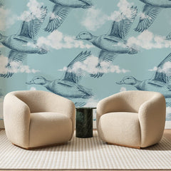 Papier peint panoramique Canards en Vol Bleu Ciel, posé sur toute la paroi d'un salon, derrière deux fauteuils en bouclette crème et un guéridon en marbre vert