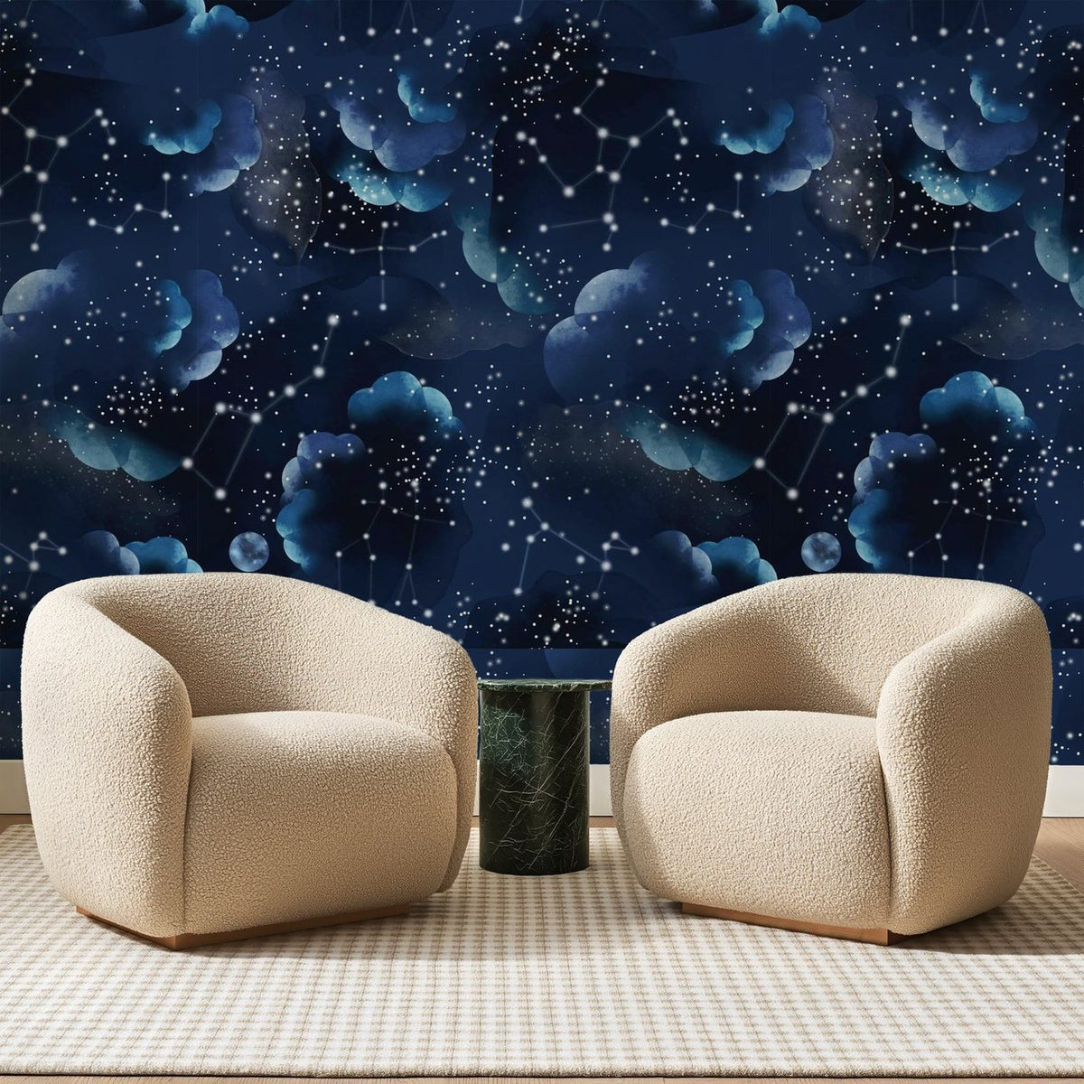 Papier peint panoramique Ciel Étoilé Bleu Nuit, posé sur toute la paroi d'un salon, derrière deux fauteuils en bouclette crème et un guéridon en marbre vert