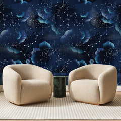Papier peint panoramique Ciel Étoilé Bleu Nuit, posé sur toute la paroi d'un salon, derrière deux fauteuils en bouclette crème et un guéridon en marbre vert