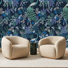 Papier peint panoramique Paon Fleuri Bleu Nuit, posé sur toute la paroi d'un salon, derrière deux fauteuils en bouclette crème et un guéridon en marbre vert