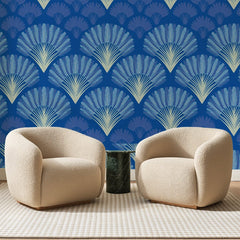 Papier peint panoramique Éventails Art Déco Bleu Roi, posé sur toute la paroi d'un salon, derrière deux fauteuils en bouclette crème et un guéridon en marbre vert
