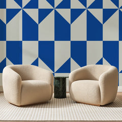 Papier peint panoramique Voiles Géométriques Bleu Roi, posé sur toute la paroi d'un salon, derrière deux fauteuils en bouclette crème et un guéridon en marbre vert