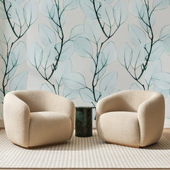 Papier peint panoramique Feuilles Aquarelle Bleu Givré, posé sur toute la paroi d'un salon, derrière deux fauteuils en bouclette crème et un guéridon en marbre vert