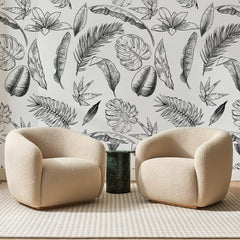 Papier peint panoramique Feuillages Tropicaux Noir et Blanc, posé sur toute la paroi d'un salon, derrière deux fauteuils en bouclette crème et un guéridon en marbre vert