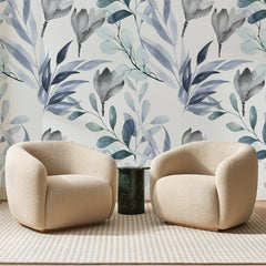 Papier peint panoramique Feuillage Aquarelle Bleu Ardoise, posé sur toute la paroi d'un salon, derrière deux fauteuils en bouclette crème et un guéridon en marbre vert