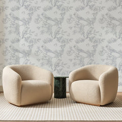 Papier peint panoramique Oiseaux Gravés Gris Perle, posé sur toute la paroi d'un salon, derrière deux fauteuils en bouclette crème et un guéridon en marbre vert