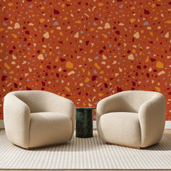 Papier peint panoramique Éclats de Terrazzo Terre Cuite, posé sur toute la paroi d'un salon, derrière deux fauteuils en bouclette crème et un guéridon en marbre vert