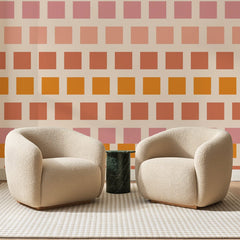 Papier peint panoramique Petits Carrés Ambre et Rose, posé sur toute la paroi d'un salon, derrière deux fauteuils en bouclette crème et un guéridon en marbre vert