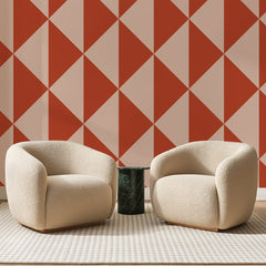 Papier peint panoramique Grands Triangles Terre Cuite, posé sur toute la paroi d'un salon, derrière deux fauteuils en bouclette crème et un guéridon en marbre vert