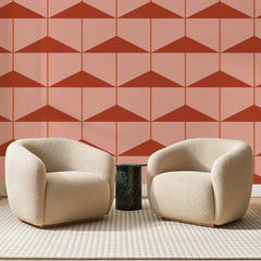 Papier peint panoramique Triangles Étagés Rose Pêche, posé sur toute la paroi d'un salon, derrière deux fauteuils en bouclette crème et un guéridon en marbre vert