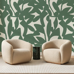 Papier peint panoramique Feuilles Découpées Sauge et Ivoire, posé sur toute la paroi d'un salon, derrière deux fauteuils en bouclette crème et un guéridon en marbre vert