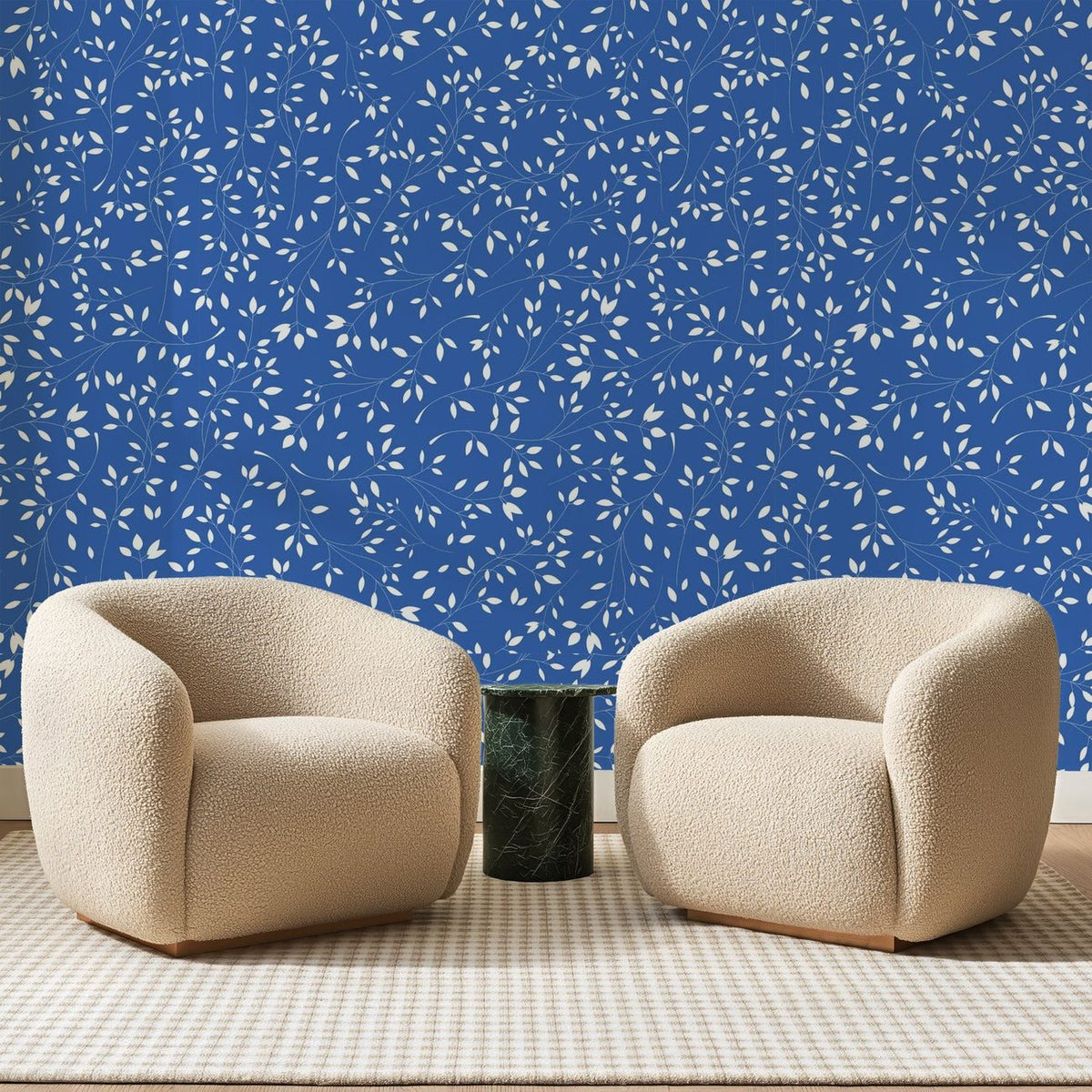 Papier peint panoramique Petites Feuilles Blanches Bleu Roi, posé sur toute la paroi d'un salon, derrière deux fauteuils en bouclette crème et un guéridon en marbre vert
