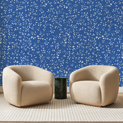 Papier peint panoramique Petites Feuilles Blanches Bleu Roi, posé sur toute la paroi d'un salon, derrière deux fauteuils en bouclette crème et un guéridon en marbre vert