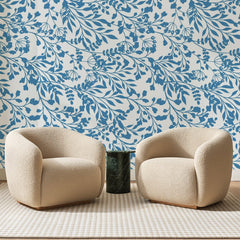Papier peint panoramique Feuillages Fins Bleu Porcelaine, posé sur toute la paroi d'un salon, derrière deux fauteuils en bouclette crème et un guéridon en marbre vert