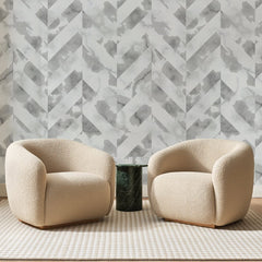 Papier peint panoramique Chevrons de Marbre Gris, posé sur toute la paroi d'un salon, derrière deux fauteuils en bouclette crème et un guéridon en marbre vert