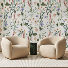Papier peint panoramique Prairie Fleurie Vert Sauge, posé sur toute la paroi d'un salon, derrière deux fauteuils en bouclette crème et un guéridon en marbre vert