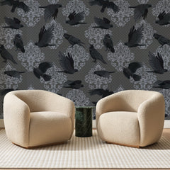 Papier peint panoramique Corbeaux sur Damas Anthracite, posé sur toute la paroi d'un salon, derrière deux fauteuils en bouclette crème et un guéridon en marbre vert