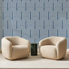 Papier peint panoramique Arcades Nervurées Bleu de Chine, posé sur toute la paroi d'un salon, derrière deux fauteuils en bouclette crème et un guéridon en marbre vert