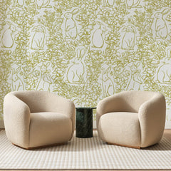 Papier peint panoramique Lapins et Feuillages Dorés, posé sur toute la paroi d'un salon, derrière deux fauteuils en bouclette crème et un guéridon en marbre vert