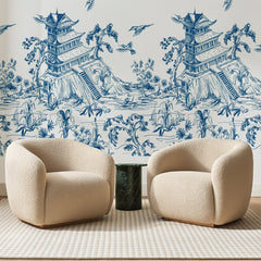 Papier peint panoramique Pagode Bleue et Cascade, posé sur toute la paroi d'un salon, derrière deux fauteuils en bouclette crème et un guéridon en marbre vert