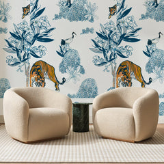 Papier peint panoramique Tigres et Grues Bleu Porcelaine, posé sur toute la paroi d'un salon, derrière deux fauteuils en bouclette crème et un guéridon en marbre vert