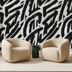 Papier peint panoramique Coups de Pinceau Noirs, posé sur toute la paroi d'un salon, derrière deux fauteuils en bouclette crème et un guéridon en marbre vert