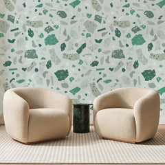 Papier peint panoramique Terrazzo Vert d'Eau, posé sur toute la paroi d'un salon, derrière deux fauteuils en bouclette crème et un guéridon en marbre vert