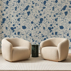 Papier peint panoramique Éclaboussures Bleues sur Écru, posé sur toute la paroi d'un salon, derrière deux fauteuils en bouclette crème et un guéridon en marbre vert