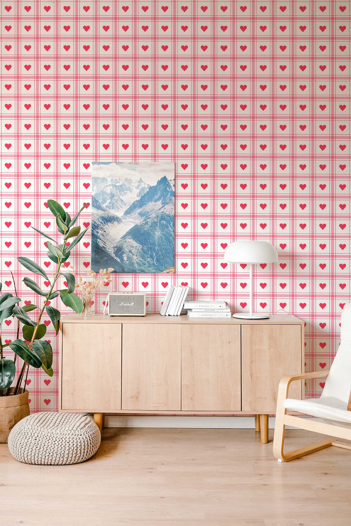 Mur de salon tapissé du vichy rose à cœurs, buffet en bois clair et fauteuil en bois.